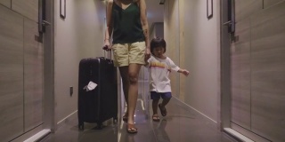 亚洲母亲和她的儿子拉着手提箱在酒店走廊。