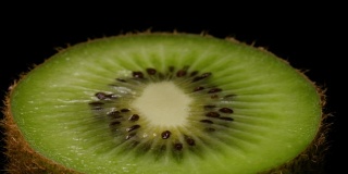 猕猴桃在转盘上旋转的微距拍摄。一个多汁的绿色猕猴桃切成两半，孤立在黑色背景上的特写。