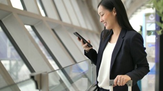微笑的年轻亚洲女子在机场使用智能手机视频素材模板下载