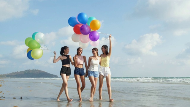 一群朋友拿着彩色气球沿着海滩散步。