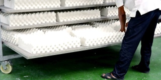 男人在工厂的架子上摆放白色乳胶枕头