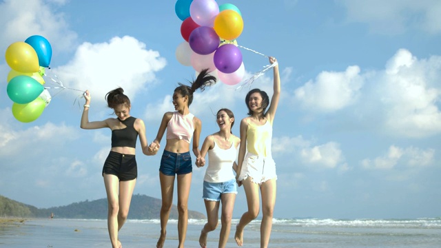 潮人朋友们拿着彩色气球走在海滩上，心情愉快。有聚会庆祝观念的人。4 k决议。慢动作镜头。