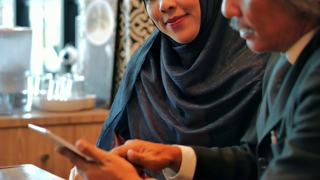 亚洲穆斯林商务团队在一家咖啡馆用平板电脑开会。商务人士会议伙伴关系。商务顾问在会议期间分析公司的财务数据。商务人士科技与团队合作理念。阿拉伯青年