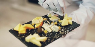 餐厅里的服务员手里拿着一块黑色的木板，上面有各种各样的硬奶酪，上面点缀着水果和芝麻。