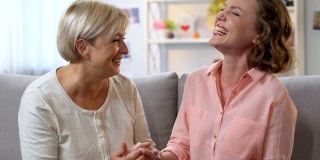 妈妈和女儿在沙发上大笑，分享好消息，互相信任的谈话