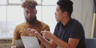 两名男性创意人员正在用笔记本电脑和平板电脑与一位看不见的同事开会