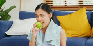 年轻的亚洲女子吃青苹果后在家客厅锻炼，人与健康的生活方式，幸福