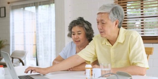 亚洲夫妇老年人使用笔记本电脑视频会议与医生有关的疾病和处方药丸在家里的客厅。健康的生活方式。居家养老概念