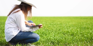 现代农妇，一个年轻开朗的企业家在麦田里行走的慢镜头，使用数字平板电脑。春天，农业职业，小型企业，投资，创新，女性领导者工作，使用技术，户外。