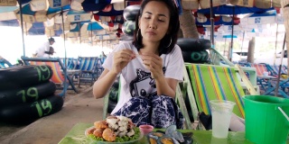 年轻的亚洲女人吃海鲜和木瓜沙拉泰国食物在海滩。快乐的情绪。