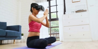 亚洲女人用虚拟现实眼镜耳机在家里客厅地板上在线训练瑜伽姿势的慢动作。自我学习。广角镜头
