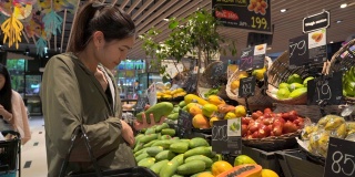 美丽的年轻女子购买水果和蔬菜在农产品部门