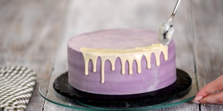 在厨房准备蛋糕的特写镜头，在蛋糕上浇白巧克力釉。