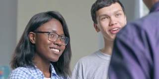 两个大学生，非洲女孩和亚洲男孩向面熟的老师提问，在休息中听他的回答，并被他的笑话逗乐