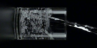垂直和慢动作:将水倒入一个饮用玻璃在黑色背景。