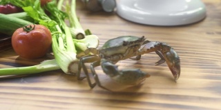 螃蟹在海鲜餐厅厨房的木桌上爬行。活螃蟹在餐桌上奔跑，食物配料为背景。海鲜的概念