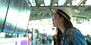 一个漫不经心的年轻女人在候机楼看航班时刻表。年轻妇女独自乘飞机旅行。