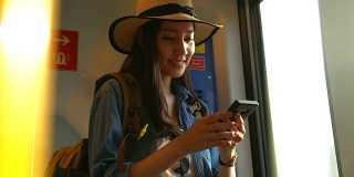 穿着旅行服装的亚洲女性在火车上玩移动设备。