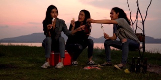 三个女人在日落时分露营时吃着棉花糖和零食