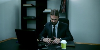 紧张的商人坐在办公室里的笔记本电脑后面，男员工看着手机，生气，慢动作
