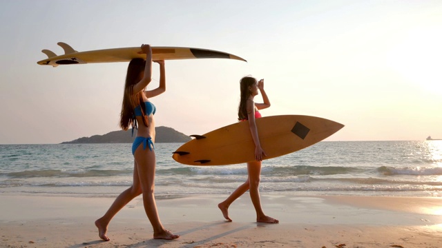 两个美丽的性感的年轻女子冲浪女孩在比基尼与冲浪板在海滩日落或日出。假期——iStock