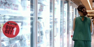 年轻美丽的亚洲女人在超市的冰箱里选择冰淇淋。