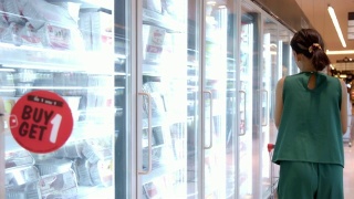 年轻美丽的亚洲女人在超市的冰箱里选择冰淇淋。视频素材模板下载
