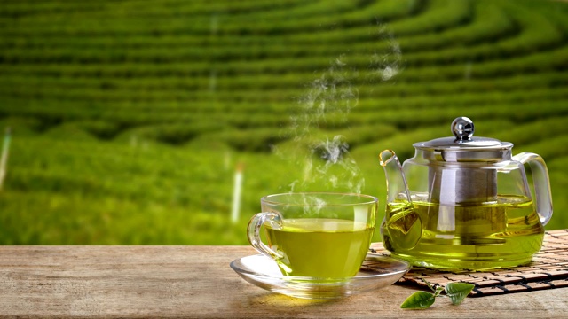 一杯热腾腾的绿茶和玻璃罐和绿茶在木桌和茶园的背景