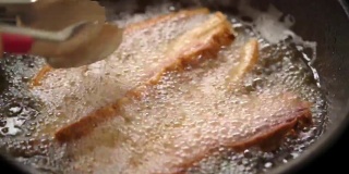 FHD Video CU SLO MO慢动作选择性聚焦稳定近距离微距拍摄妇女手煮新鲜自制油炸酥脆的猪肉腩在滚烫的棕榈油煎锅。