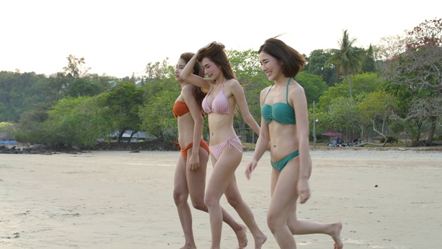 一群快乐的女孩朋友穿着比基尼在海滩上跑步，快乐的女人在暑假游客群。缓慢的运动。