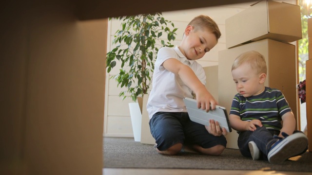 两个小男孩在他们的新房子玩或阅读平板电脑的肖像。兄弟们对使用和玩数字平板电脑很感兴趣。教育、抵押、住房和房地产概念。