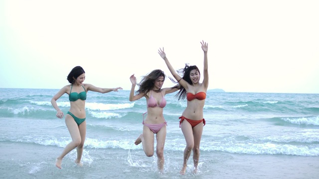 一群快乐的女孩朋友在沙滩上玩水。美丽的亚洲女孩在暑假。庆祝和放松的概念。