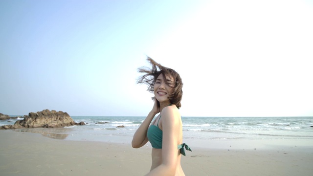 近距离拍摄的美丽的年轻亚洲女子在比基尼微笑，看着相机在热带海滩。缓慢的运动。夏季，旅游和美丽的概念。