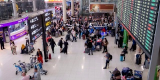 在机场航站楼，拥挤的乘客带着行李站在登机板前的4K时间间隔。晚上一群人在机场候机楼里散步