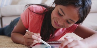 一个十几岁的女孩躺在客厅的地板上用着平板电脑和手写笔，特写