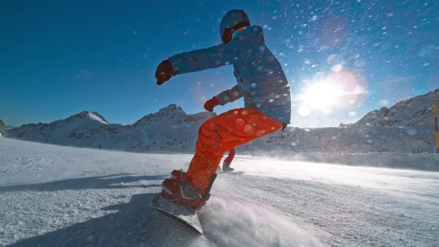 SLO MO TS滑雪板在一个阳光明媚的日子里，在一个朋友后面滑下雪道