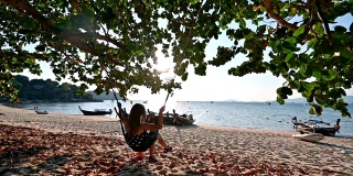 年轻女子在海滩上的木秋千上休息在树荫下