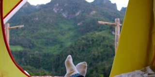 放松女人躺下和交叉腿上的毯子在帐篷和看日落时间在露营度假的山景