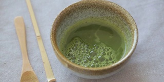 男人在一个碗里准备抹茶在蓝色的表面。饮料是抗氧化剂和多酚的丰富来源。
