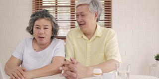 亚洲老夫妇在客厅用笔记本电脑与医生讨论医药信息，夫妇在家里躺在沙发上一起使用时间。老年人家庭健康在家的概念。