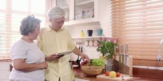 亚洲老夫妇在厨房用药片准备配料做饭，夫妇在家里用有机蔬菜做健康食品。生活方式高级家庭在家制作食物的概念。