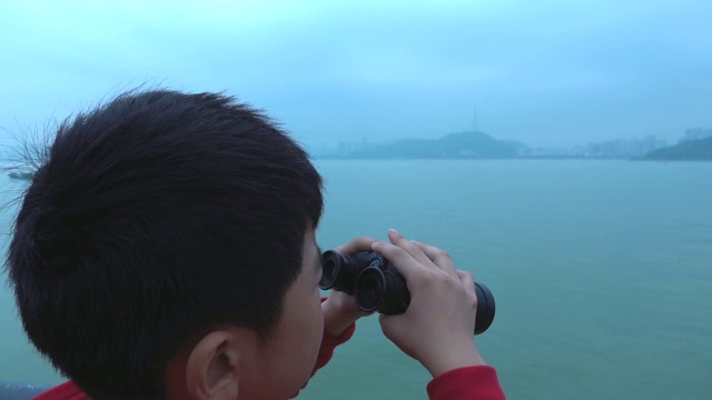 小男孩在游船上用双筒望远镜看