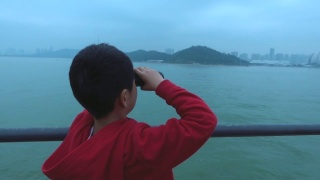 小男孩在游船上用双筒望远镜观察城市景观视频素材模板下载