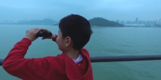 小男孩在游船上用双筒望远镜观察城市景观
