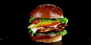 在黑色背景的木板上旋转着一个汉堡，上面有一大块肉、蔬菜和奶酪