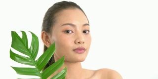 亚洲美丽的女人拿着绿叶触摸她的脸