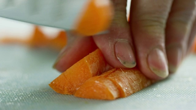 一位年长的白人妇女用菜刀在切菜板上切胡萝卜