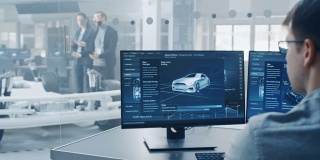 专业工程师在电脑上工作与3D软件，而同事检查电动汽车底盘原型车轮，电池和发动机站在一个高科技开发实验室。