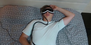 年轻帅哥用眼部按摩器，躺在床上，拿着遥控器