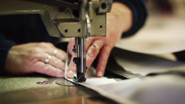 一个白人妇女的手引导一个工业缝纫机的压脚在室内制造设施缝织物